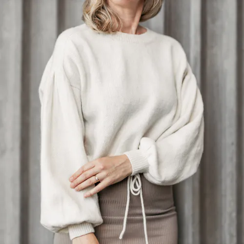 Woman wearing an off white sweater with one hand on the other arm